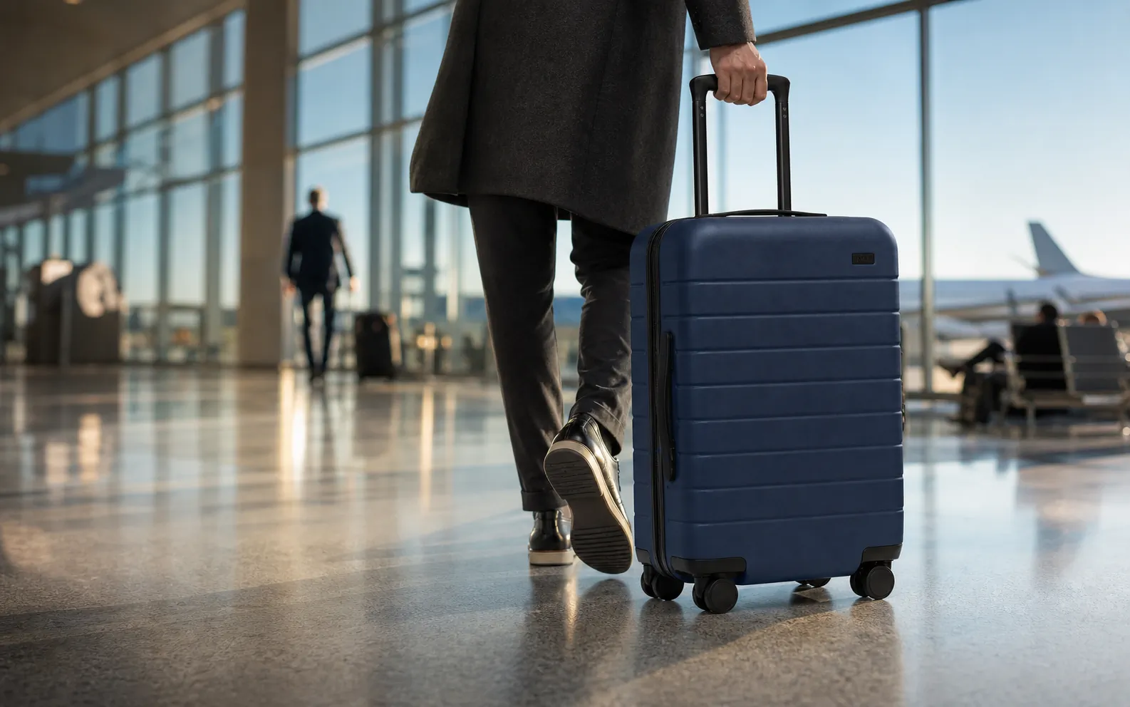 Away The Carry-On in Navy moving through a bright airport concourse in the morning.