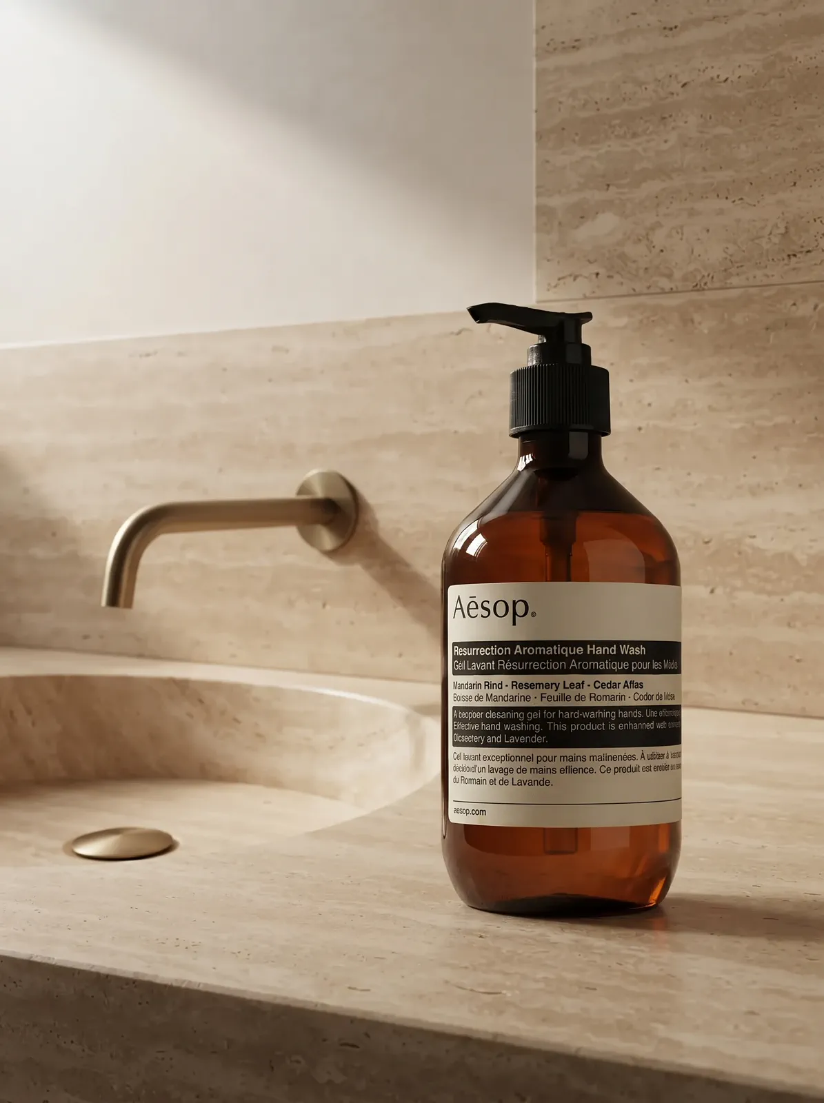 An amber pump bottle in a warm travertine hand-care setting with calm negative space.