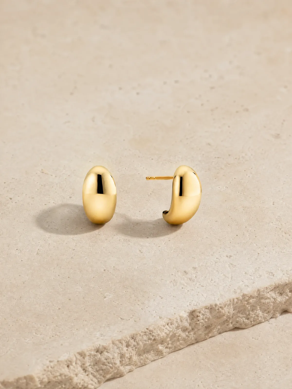 A pair of polished gold earrings spaced to show their front, curve, and post.
