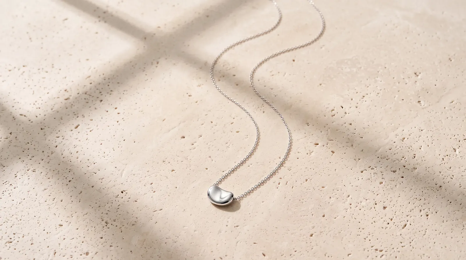 A silver pendant kept complete and centered in a clean pale-stone landscape composition.