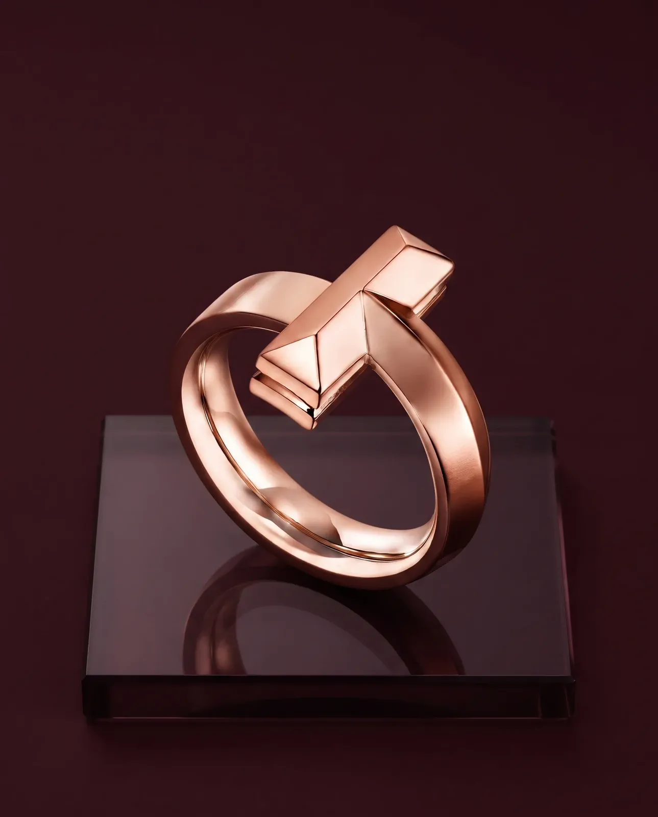 A rose-gold sculptural ring separated from a deep aubergine setting with controlled highlights.