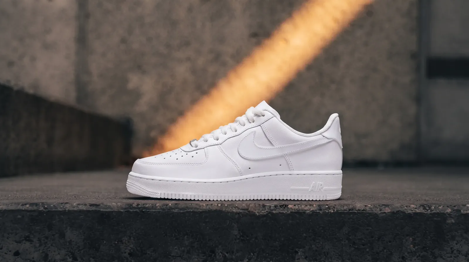 A complete white leather low-top shoe in a wide concrete campaign composition.